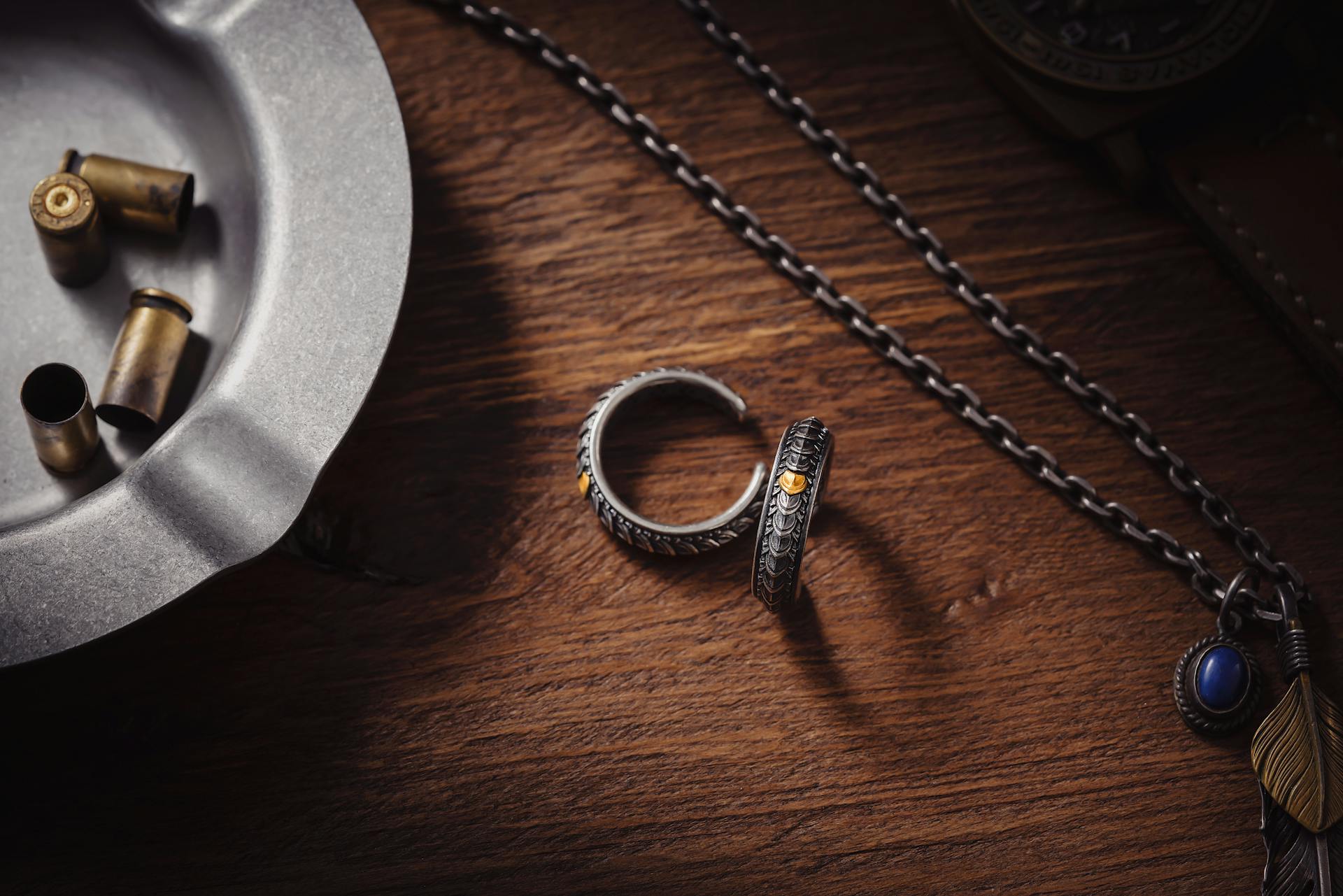 Artistic display of dragon scale cuff rings with an ashtray and chain on a wooden desk.