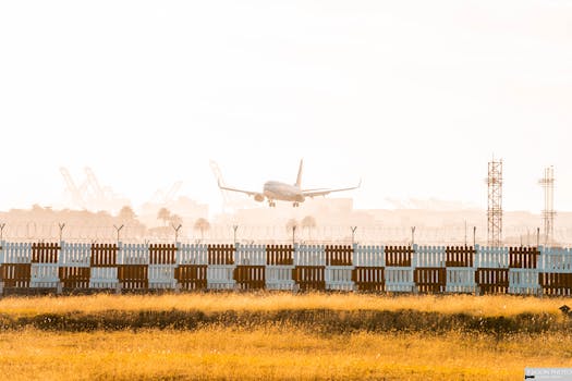 Commercial airplane lands amidst sunlight and fog at an airport runway.