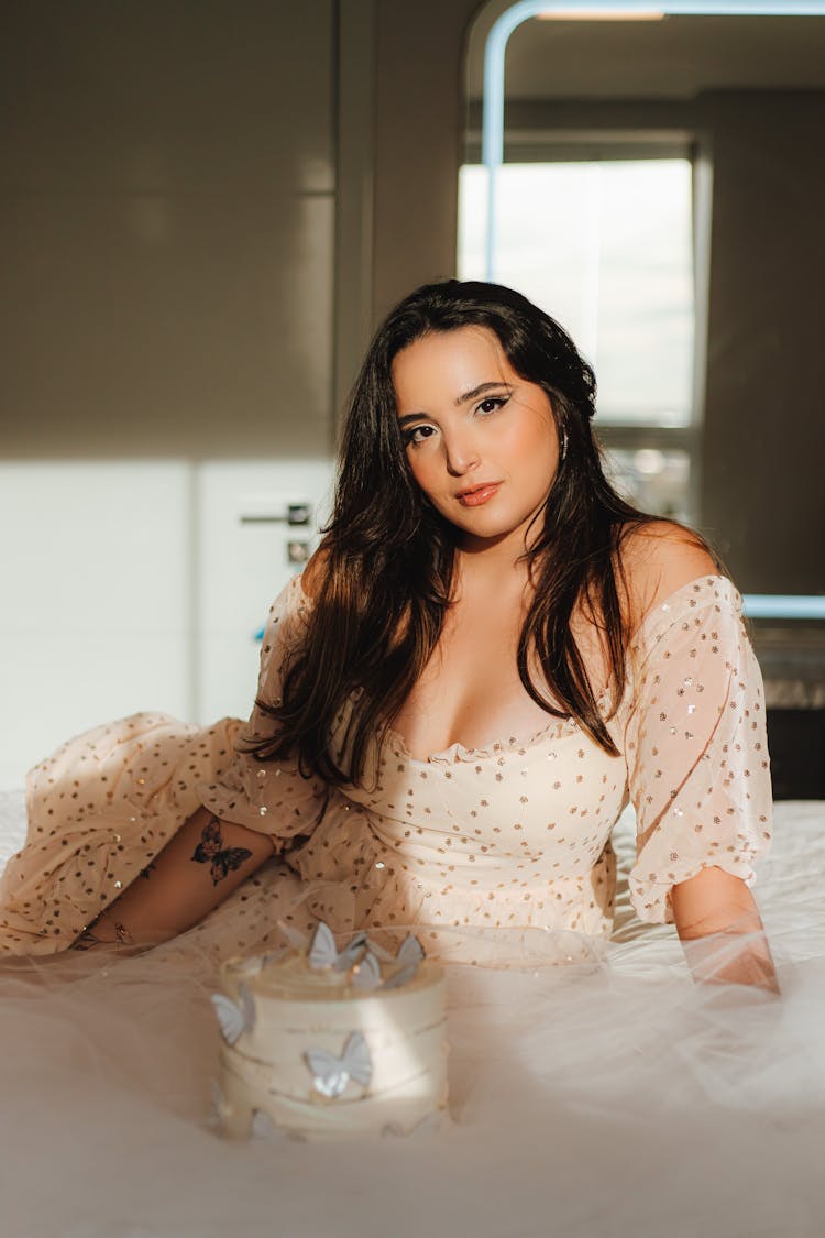 Young Woman In Dress With Birthday Cake Sitting On Bed