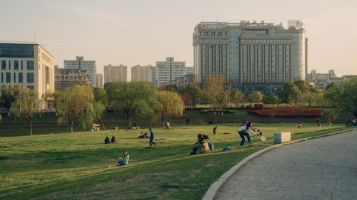 Free Sunny day in an urban park with high-rise buildings, lush greenery, and people relaxing. Stock Photo