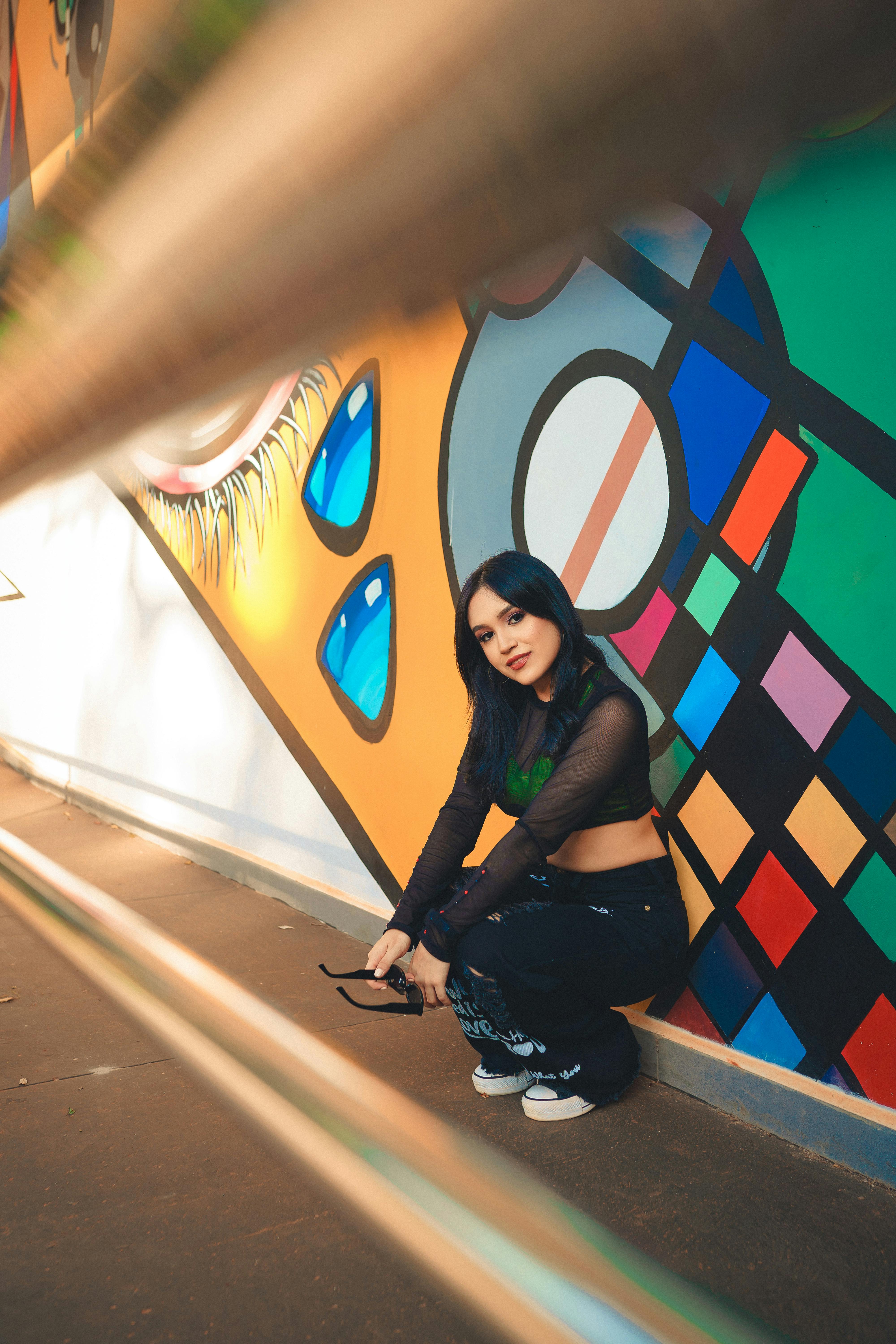 Young woman posing stylishly against vibrant graffiti wall outdoors.
