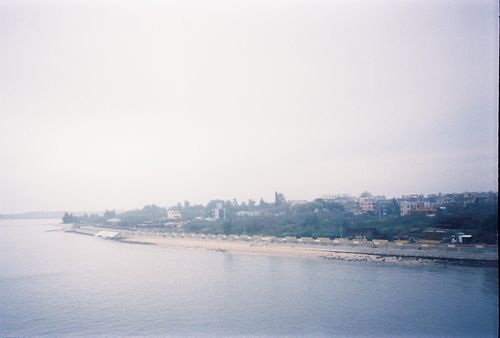 Free A serene view of an urban riverbank under overcast skies, showcasing the calm waterfront and distant cityscape. Stock Photo