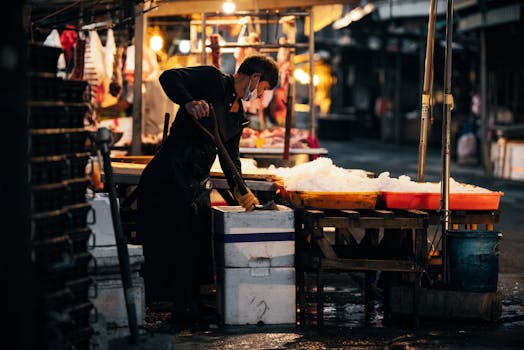 Masked vendor with shovel organizing ice in urban street market at night.