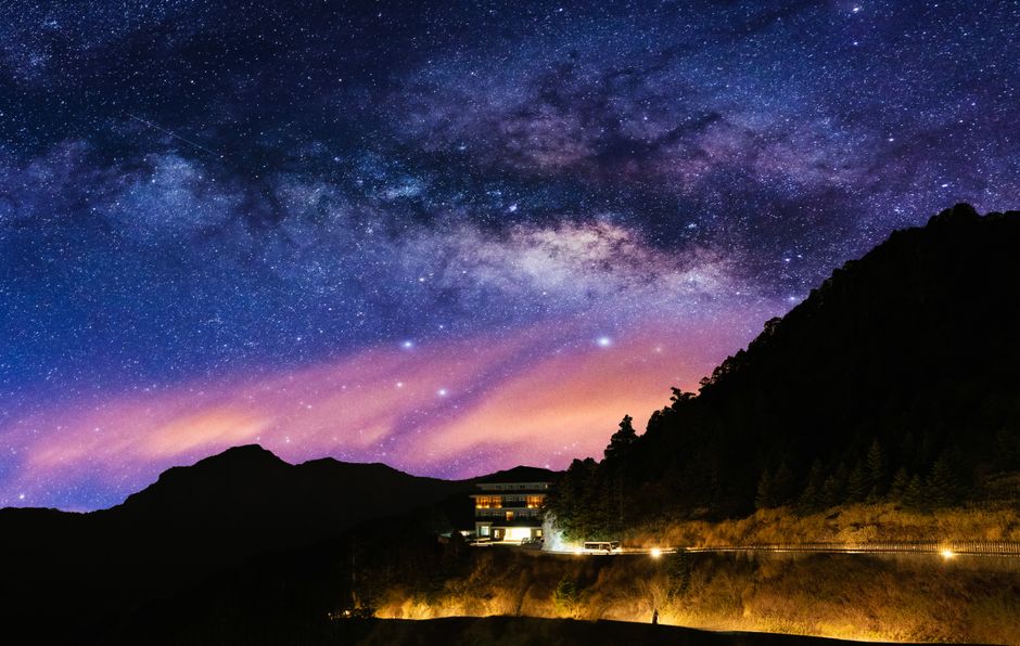 Stunning view of the Milky Way over a serene mountain landscape with a lit house at night.