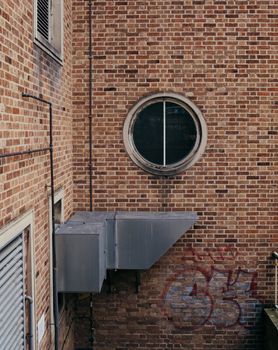 Close-up of an urban brick wall featuring a round window and graffiti.