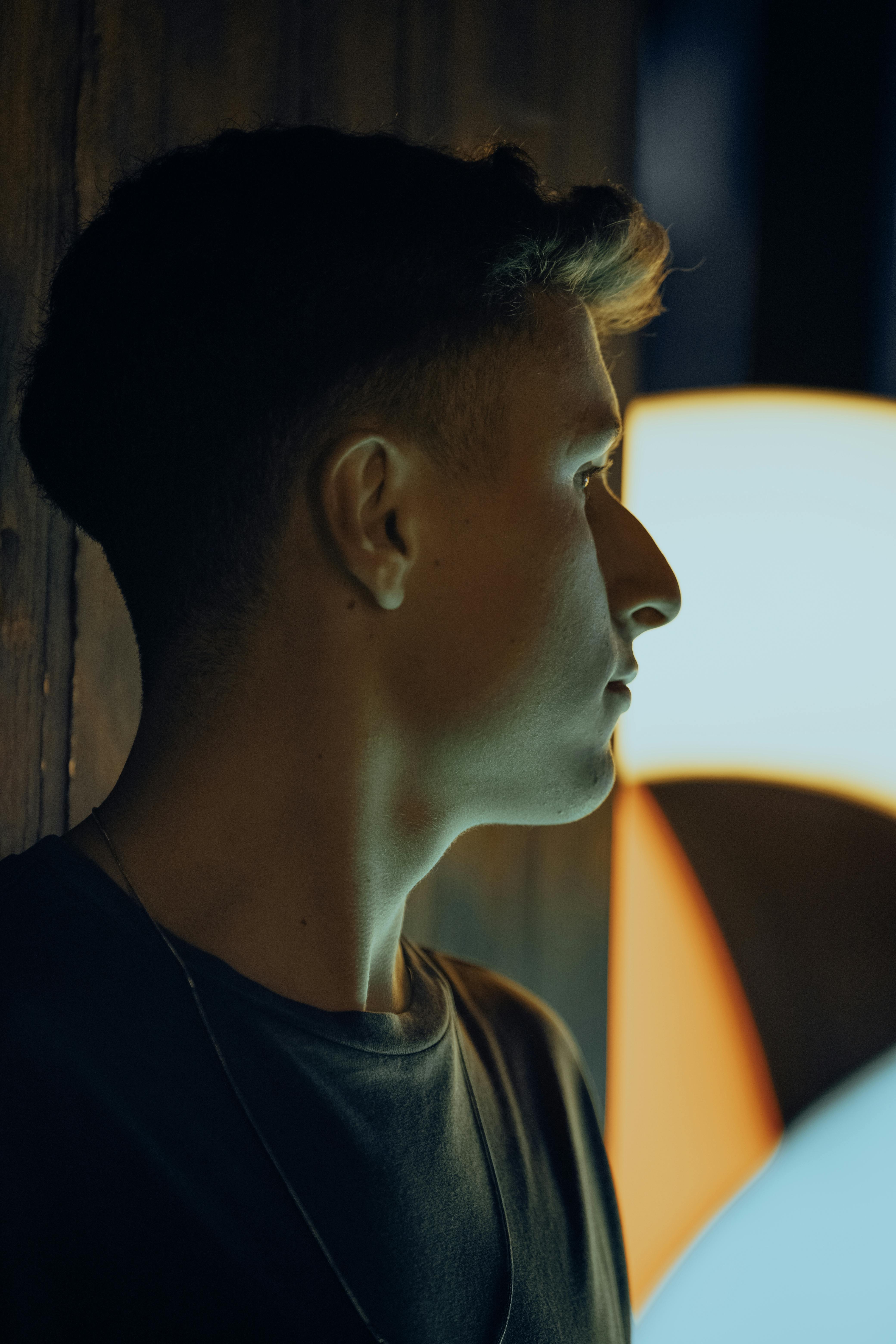 Side profile portrait of a man with short hair under artistic lighting indoors.
