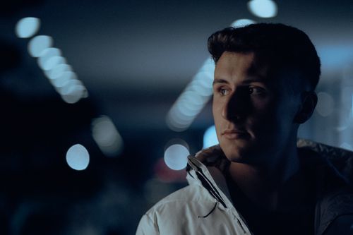 Free Pensive man in white jacket, surrounded by bokeh lights at night. Captivating urban portrait photography. Stock Photo