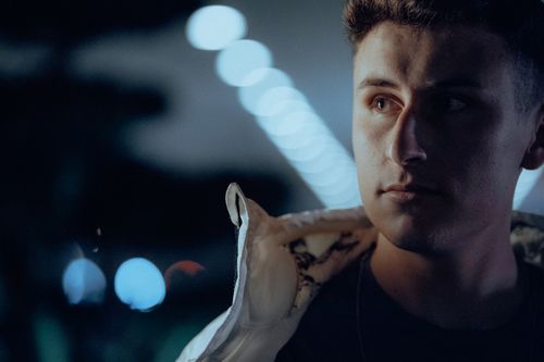 Free A contemplative man with short hair in a moody nighttime setting, illuminated by soft bokeh lights. Stock Photo