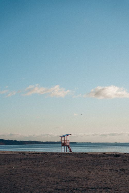 Free A lonely lifeguard tower stands on a tranquil beach under a clear blue sky. Stock Photo