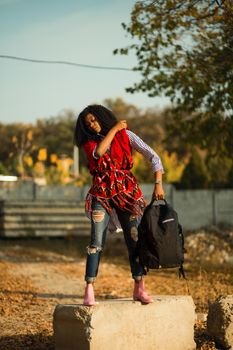 Stylish black woman posing outdoors with a backpack, showcasing fashion trends.