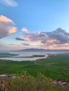 A scenic view of Qurago's lush green fields and serene lake at sunset, showcasing tranquility.