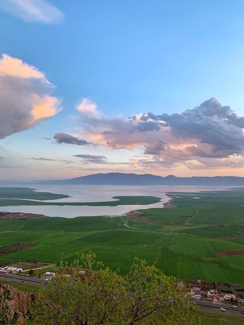 Free A scenic view of Qurago's lush green fields and serene lake at sunset, showcasing tranquility. Stock Photo