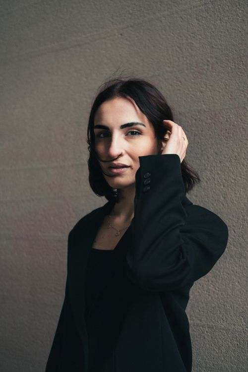 Free Portrait of a confident woman in a black suit posing against a gray wall with natural light. Stock Photo