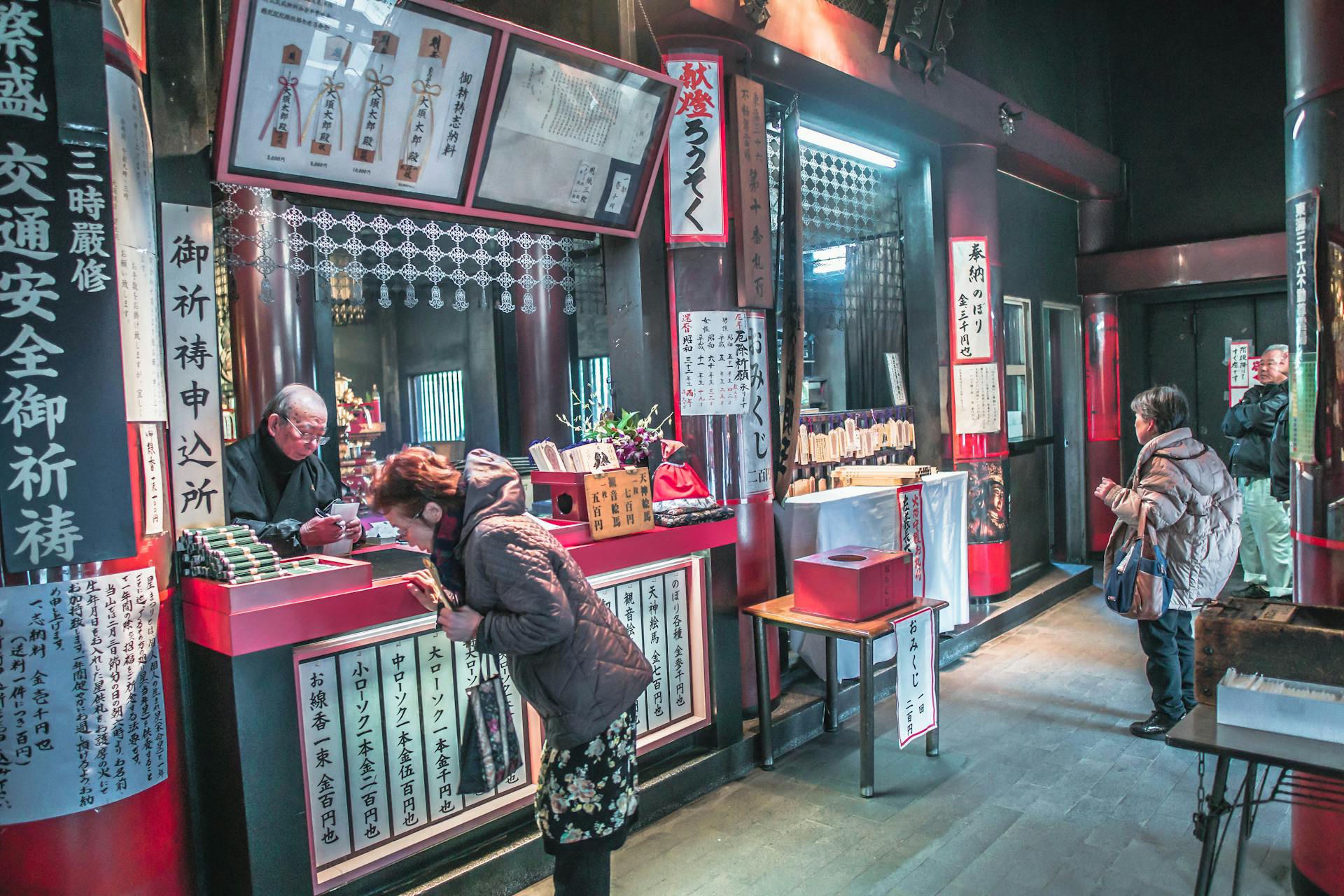 People engaging at a traditional Japanese shrine indoors, focusing on cultural practices.
