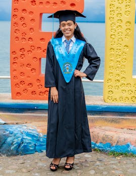 身着学术装的女毕业生在湖边色彩缤纷的户外背景旁微笑