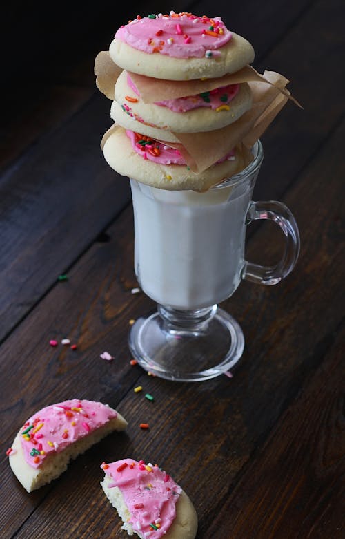 無料 牛乳と透明な短いステムフットマグの上にピンククリームとクッキー 写真素材
