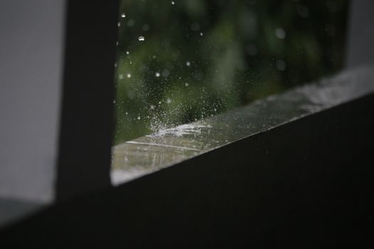 Close-up of raindrops splashing on a wet outdoor surface during rainfall.