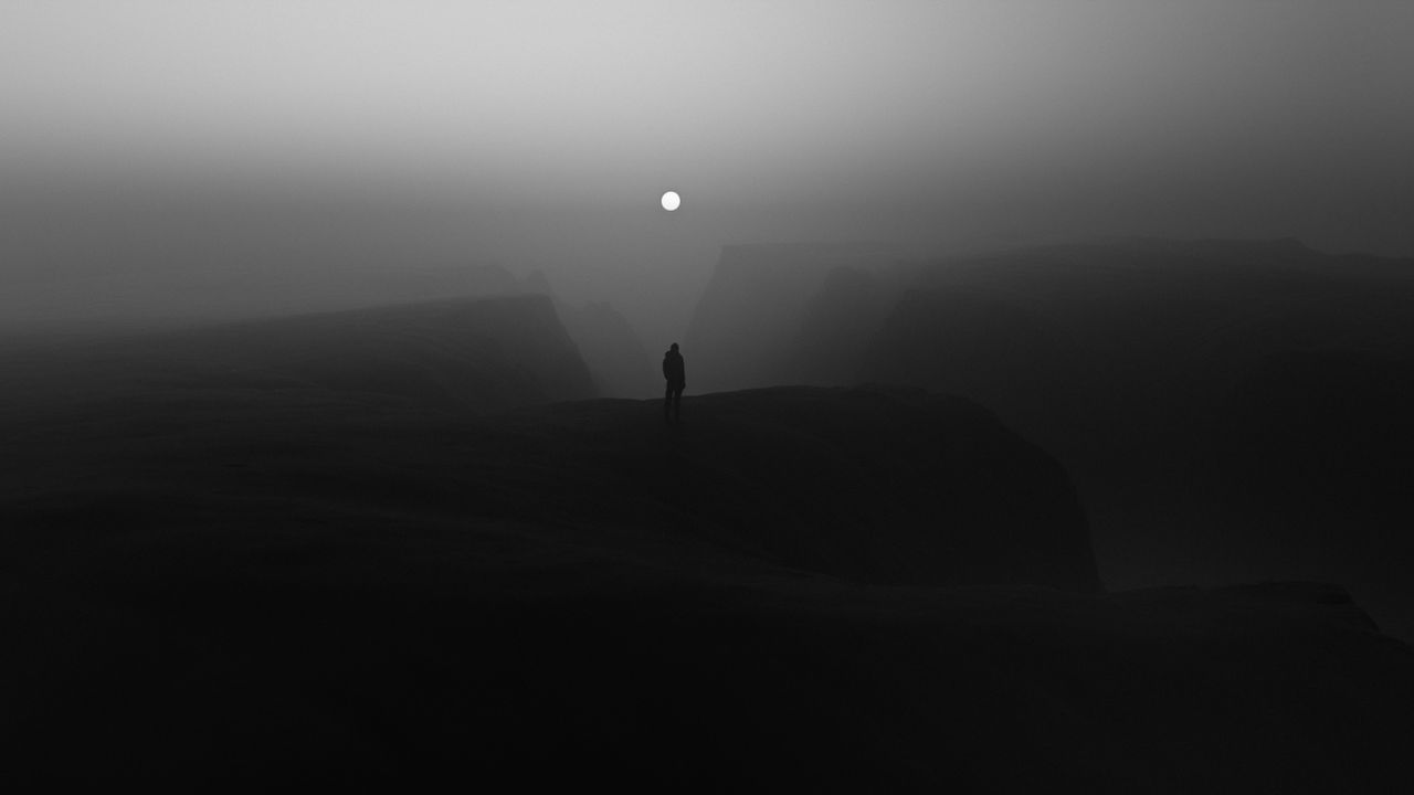 a solitary figure stands in a misty landscape under a bright moon