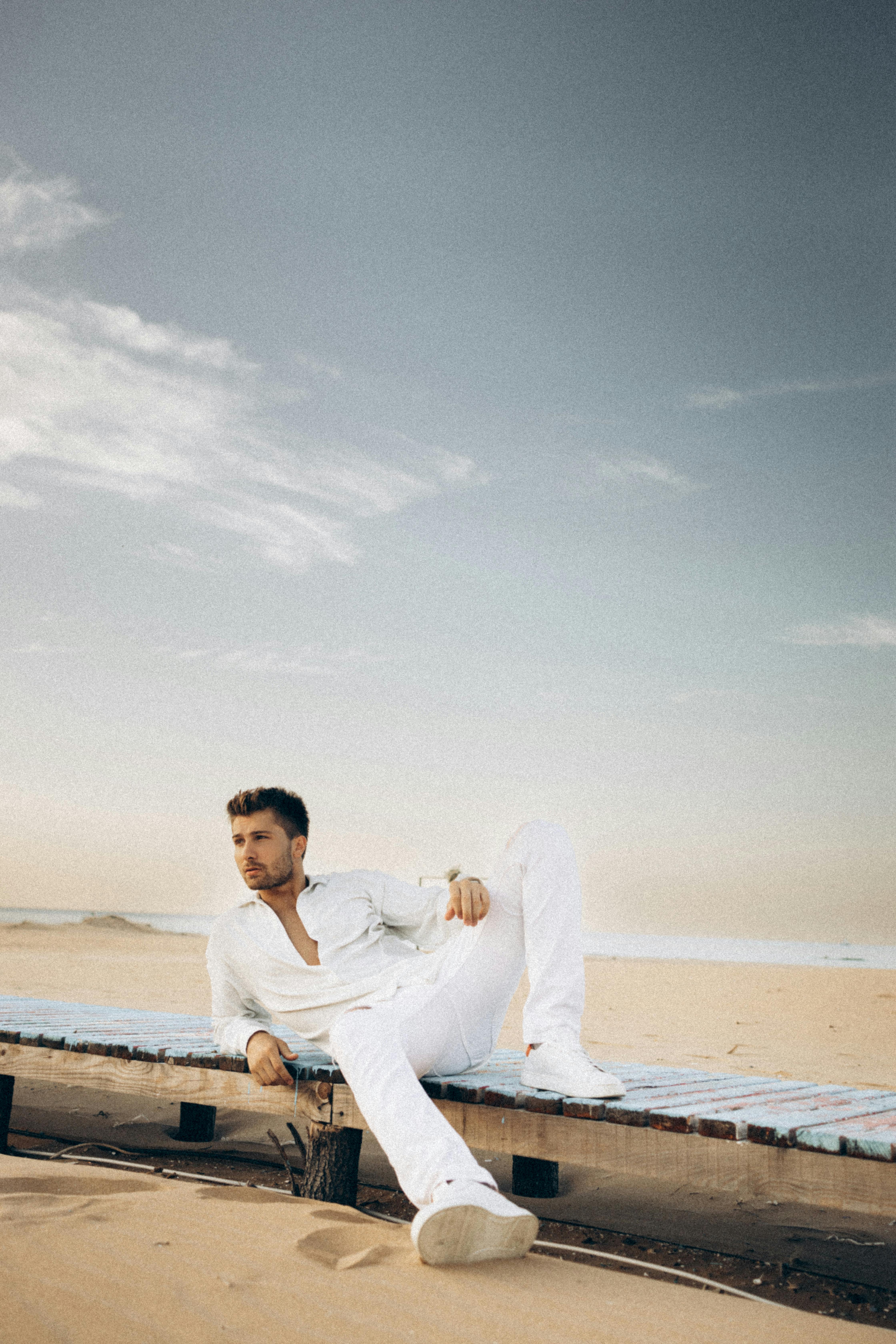 Man in white attire lounging on a Turkish beach, fashionably serene by the sea.