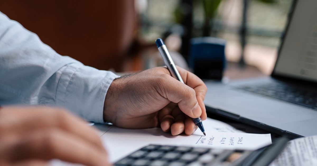 A person working through numbers with a calculator and pen at a desk with paperwork.
