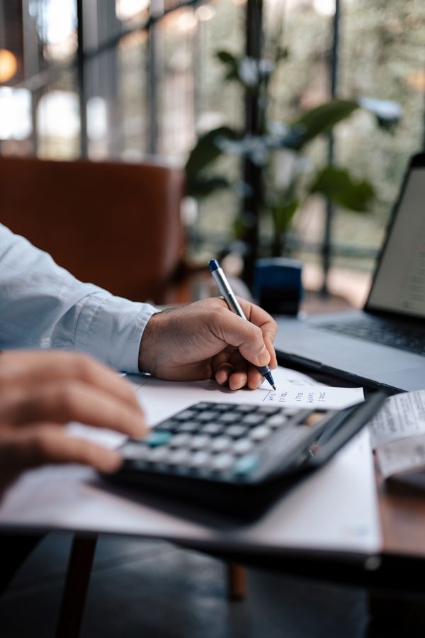 A person calculating finances with a calculator and pen on a desk