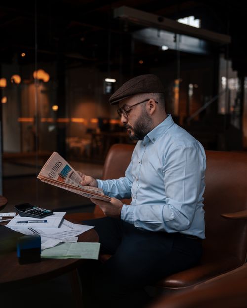 Free A stylish man reads a newspaper in a modern cafe, showcasing elegance and professionalism. Stock Photo