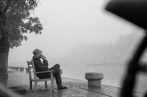 Person Smoking and Sitting by River under Fog