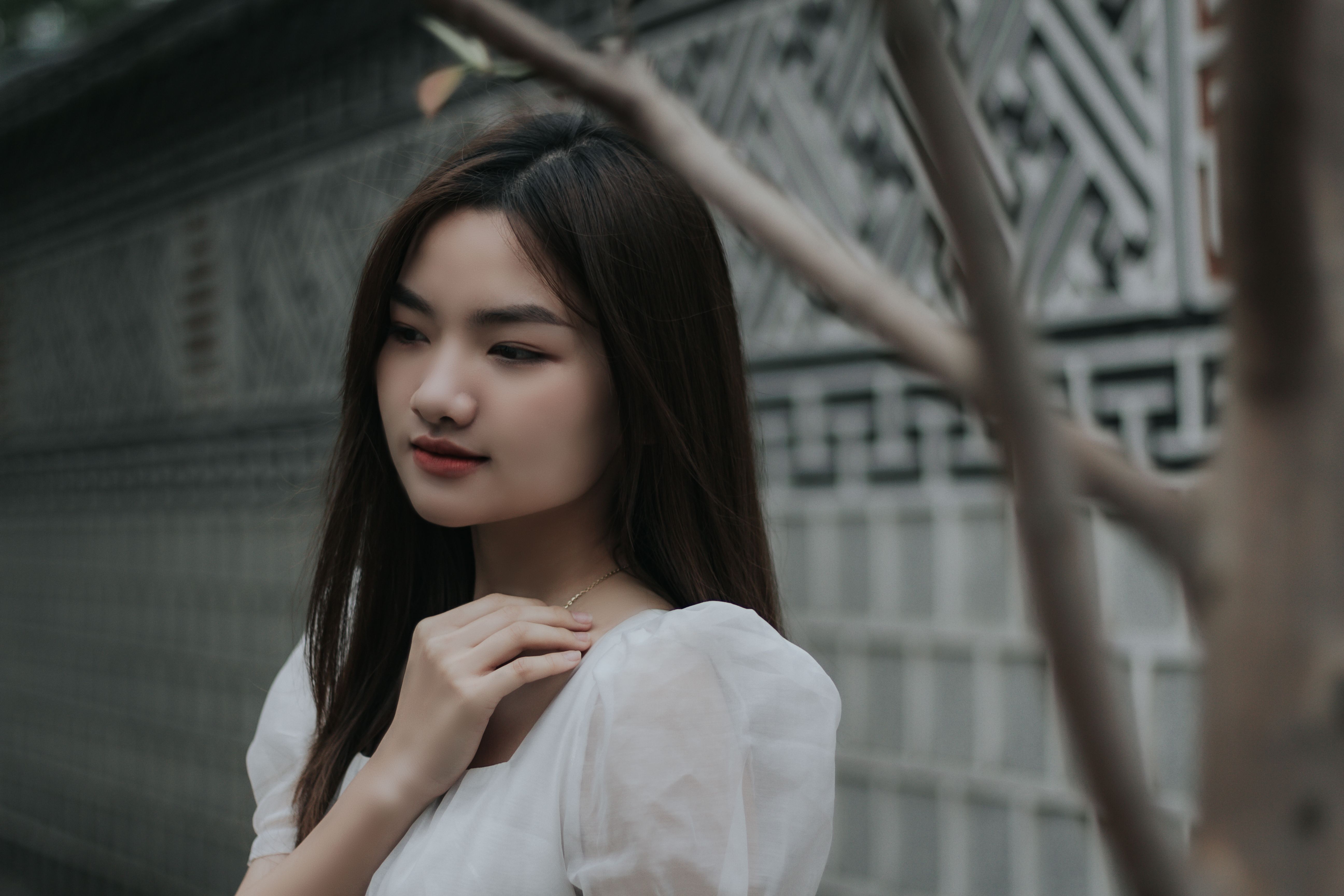 Calm and thoughtful woman with long hair posing near an intricate wall outdoors.