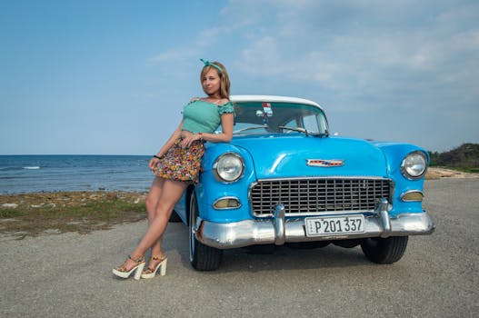 Young woman posing with a vintage Chevrolet by the ocean in summer.