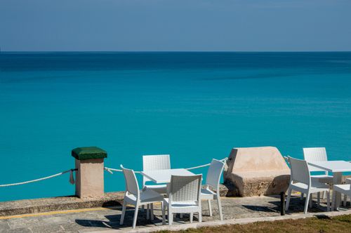 Free Relaxing outdoor patio at the seashore with white chairs and tables overlooking the turquoise ocean. Stock Photo