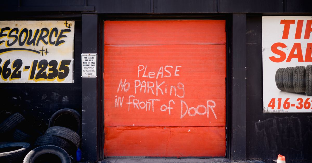 Red garage door with handwritten no parking sign surrounded by tire shop advertisements.