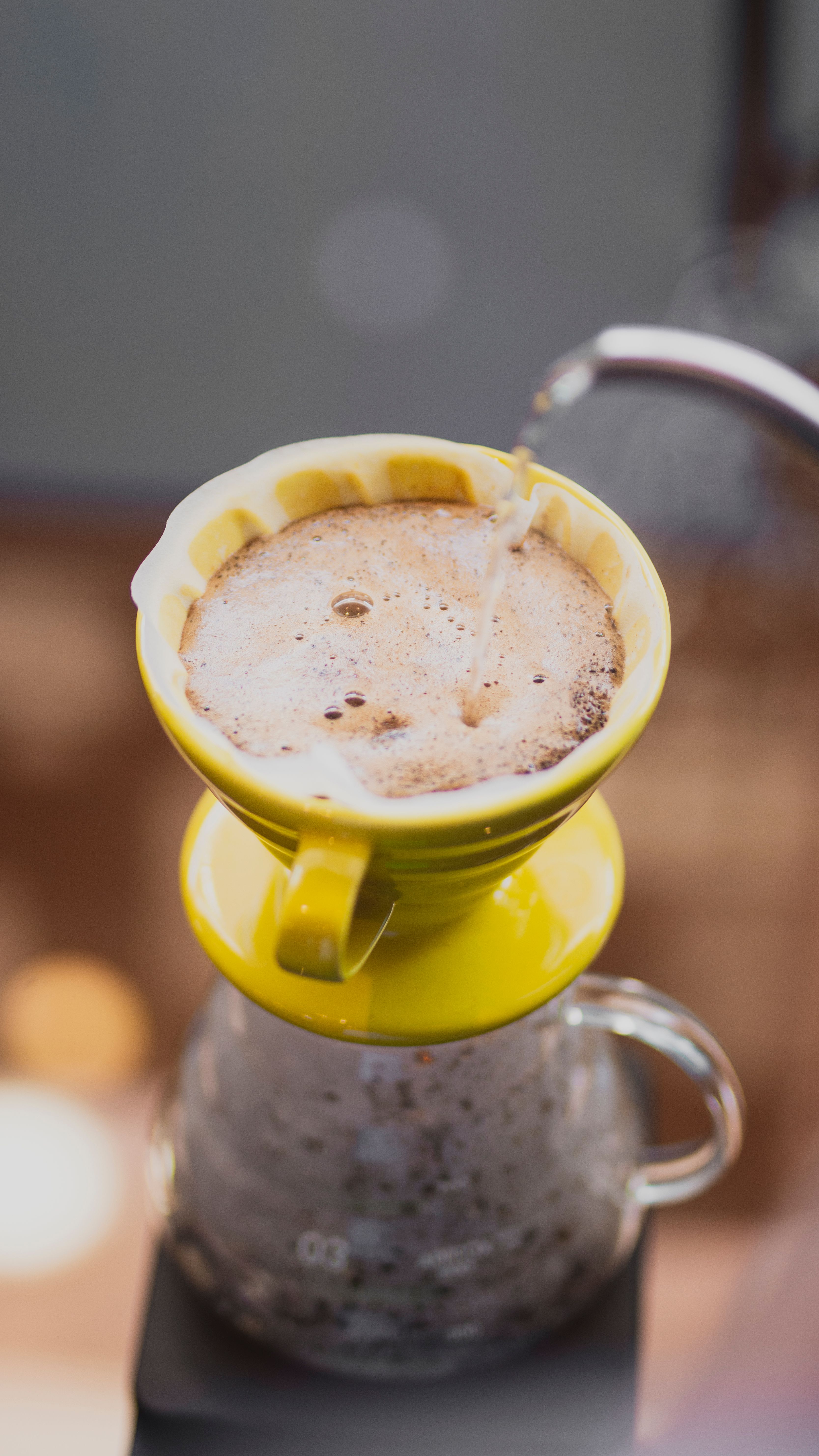 A close-up of a steaming pour-over coffee in a yellow dripper with visible foam.