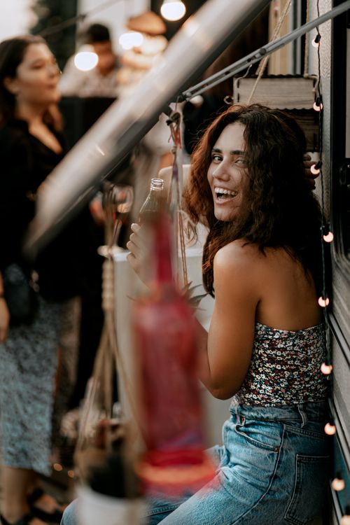 Free A woman smiling and holding a drink, enjoying a lively outdoor party in Baku, Azerbaijan at dusk. Stock Photo