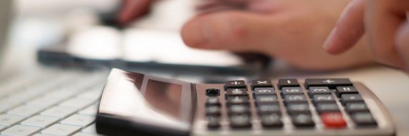 Close-up of hands using a calculator and keyboard in a financial setting, indoors.