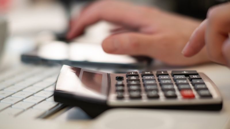 Close-up of hands using a calculator and keyboard in a financial setting, indoors.