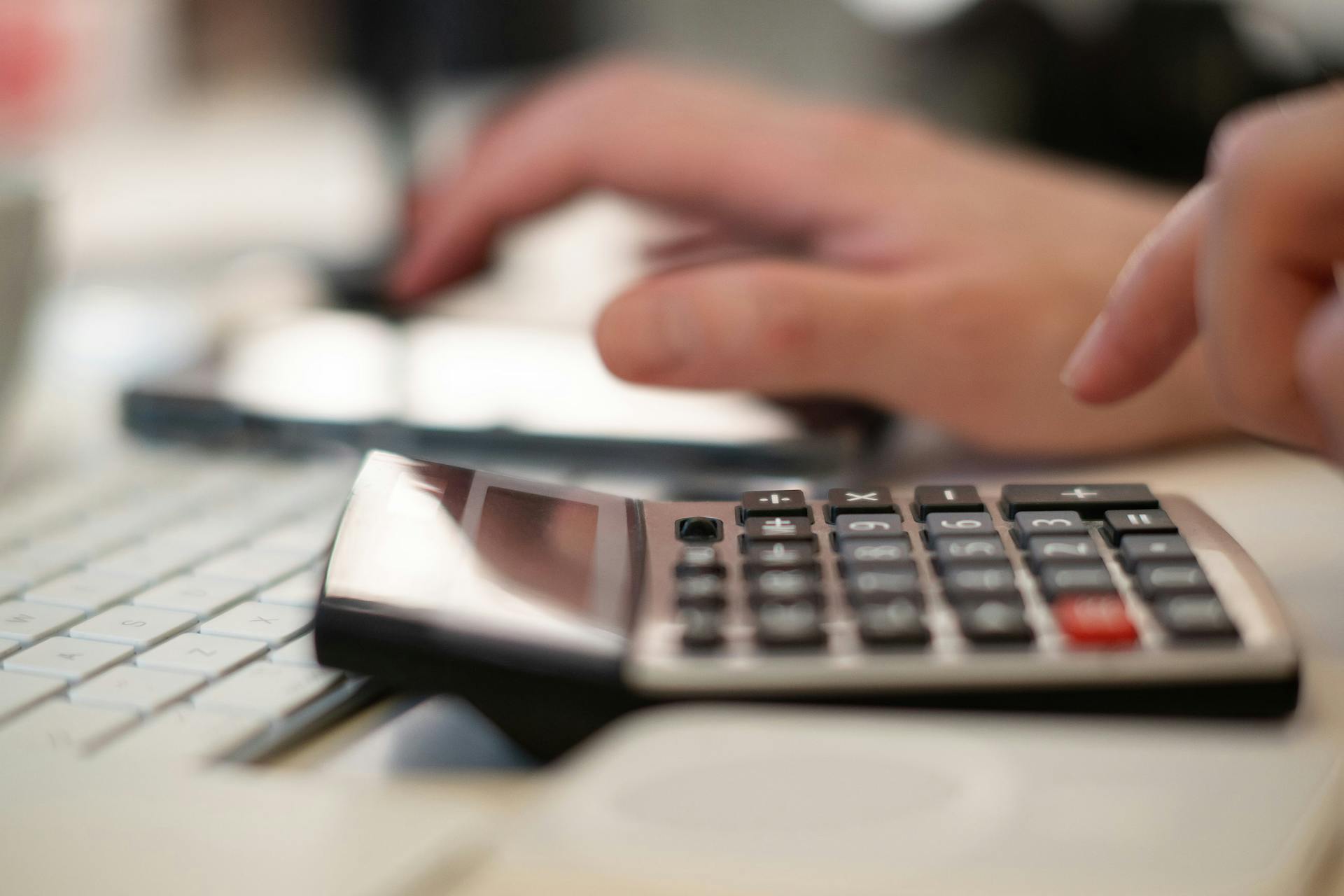 Close-up of hands using a calculator and keyboard in a financial setting, indoors.