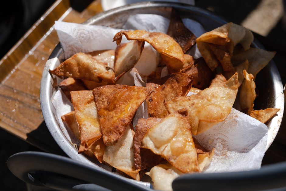 A pile of golden, fried wonton chips cut into triangles, some dusted with sesame seeds, next to a small bowl of dipping sauce.
