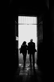 Two people in silhouette walking through a doorway backlit by bright light.