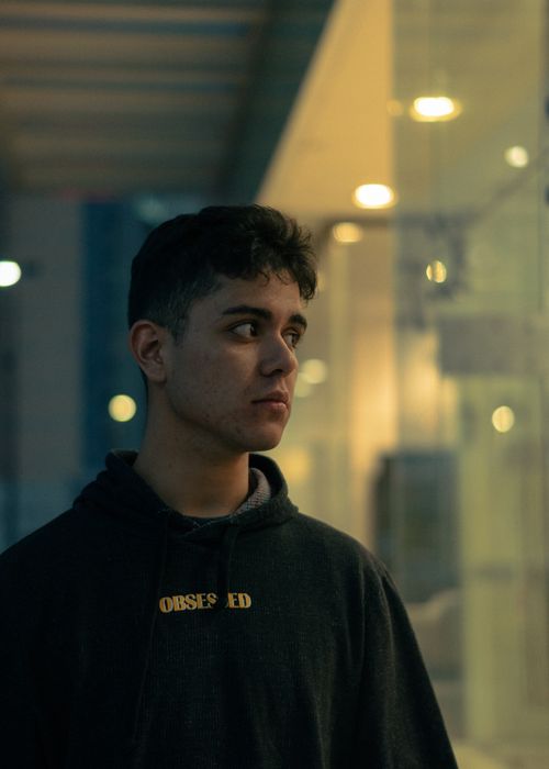 Free Young man gazing thoughtfully in an urban setting with a warm light backdrop. Stock Photo