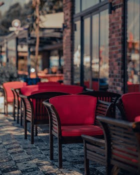 Stylish red armchairs in an outdoor dining area with glass walls and urban architecture.