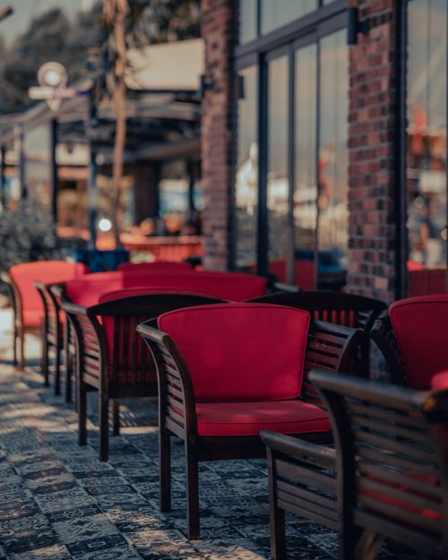 Free Stylish red armchairs in an outdoor dining area with glass walls and urban architecture. Stock Photo
