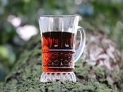 Clear glass mug filled with tea placed on mossy tree bark in a natural setting.