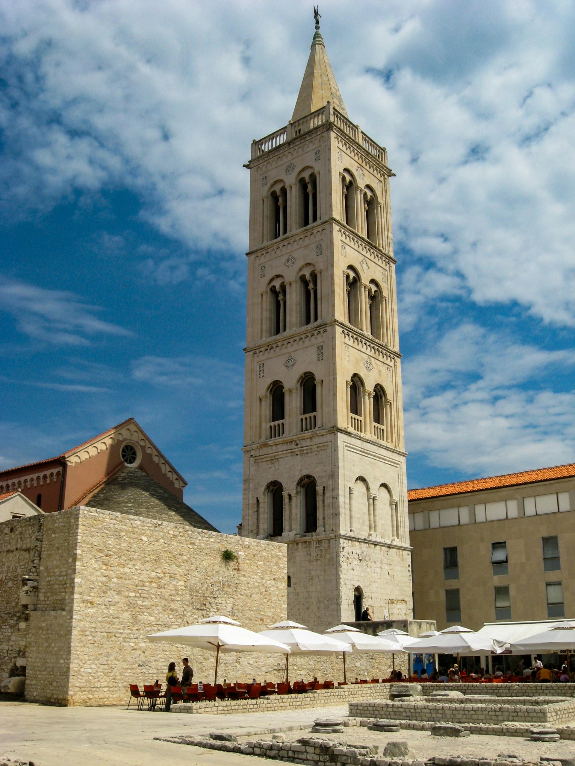 Scenic view of the historic Bell Tower of St. Anastasia in Zadar with vibrant umbrellas in the foreground. by Sun Pixel Photography