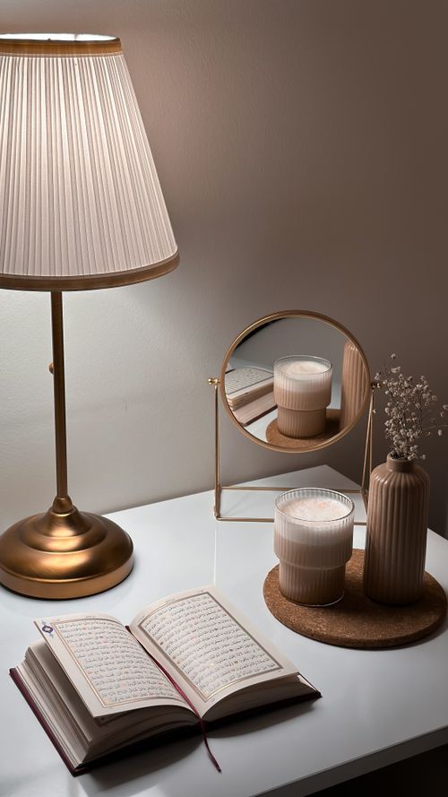 Free A cozy desk scene featuring a lamp, open book, and decorative elements like a mirror, candle, and flower vase. Stock Photo