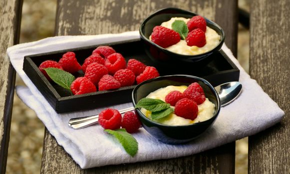 Fresh raspberries served with creamy dessert in elegant black bowls on a rustic table.
