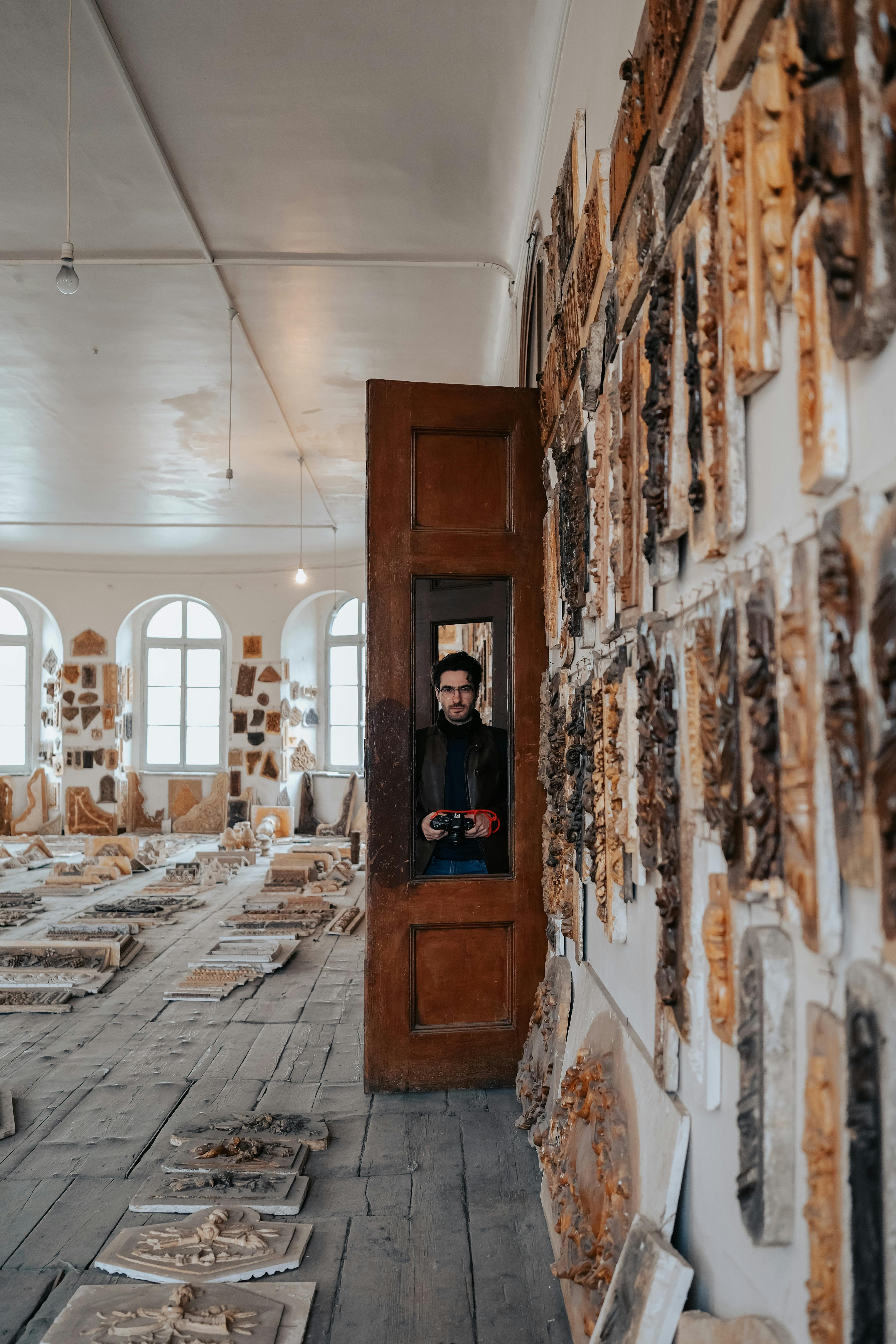 Man standing in an art and ceramic workshop with a camera, highlighting historic interior design.
