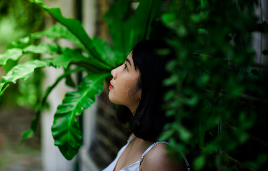 A woman gazing upwards surrounded by lush tropical plants in a peaceful outdoor setting.