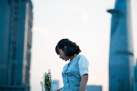 一位短发年轻女子手捧鲜花站在现代城市景观前