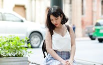 一位年轻的亚洲女性坐在城市街道上，街道两旁有汽车和建筑物