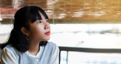 一位年轻的亚洲女孩在宁静的室内戴着耳环，若有所思地凝望着窗外